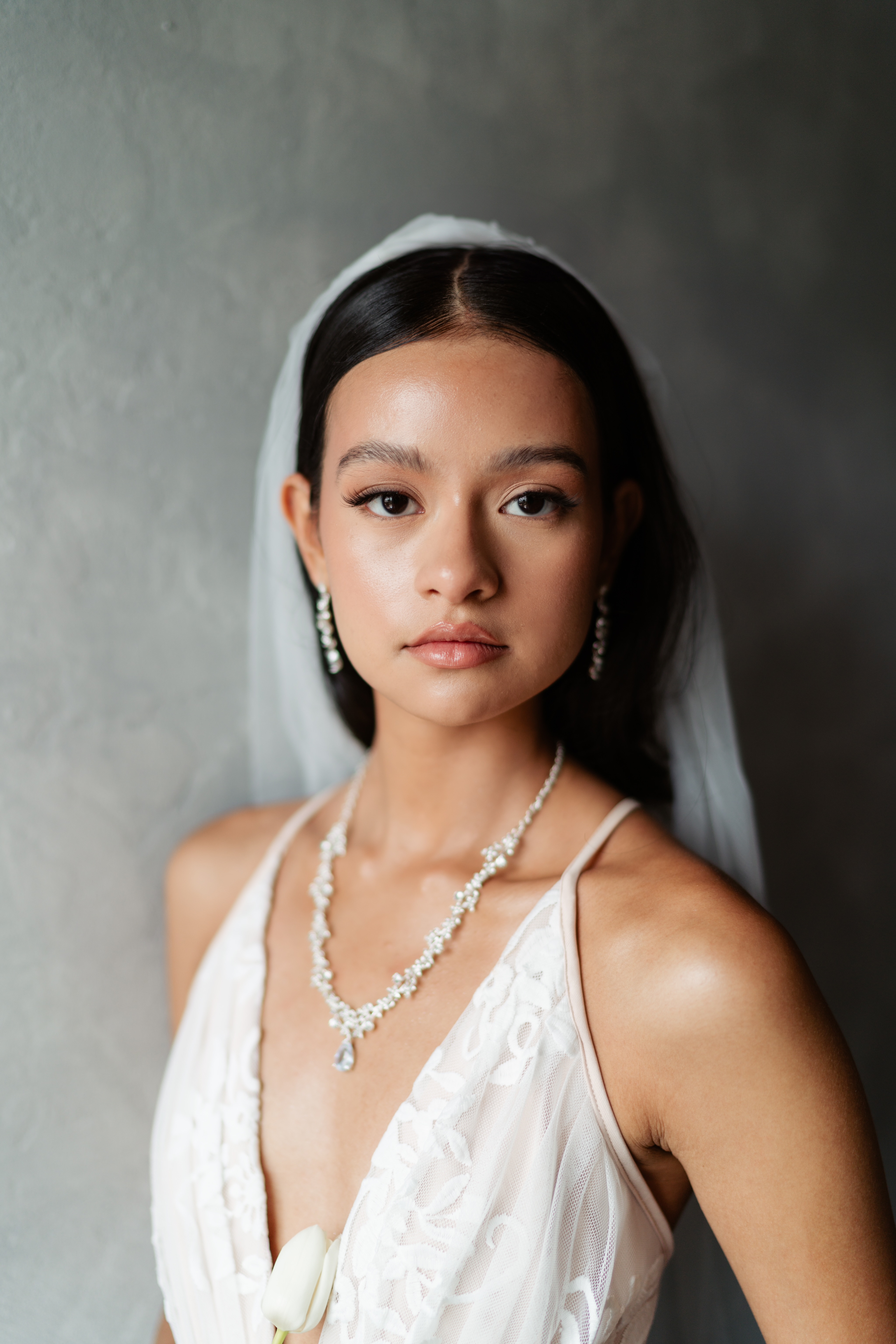 Close-up bridal portrait with a sleek veil, pearl jewelry, and polished makeup.