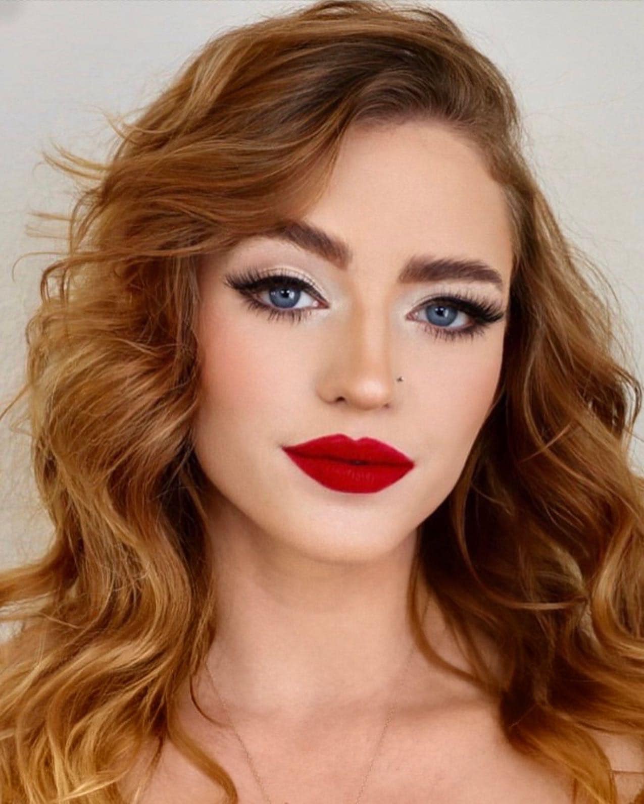 Editorial portrait with red hair, bold red lips, and graphic eye makeup.
