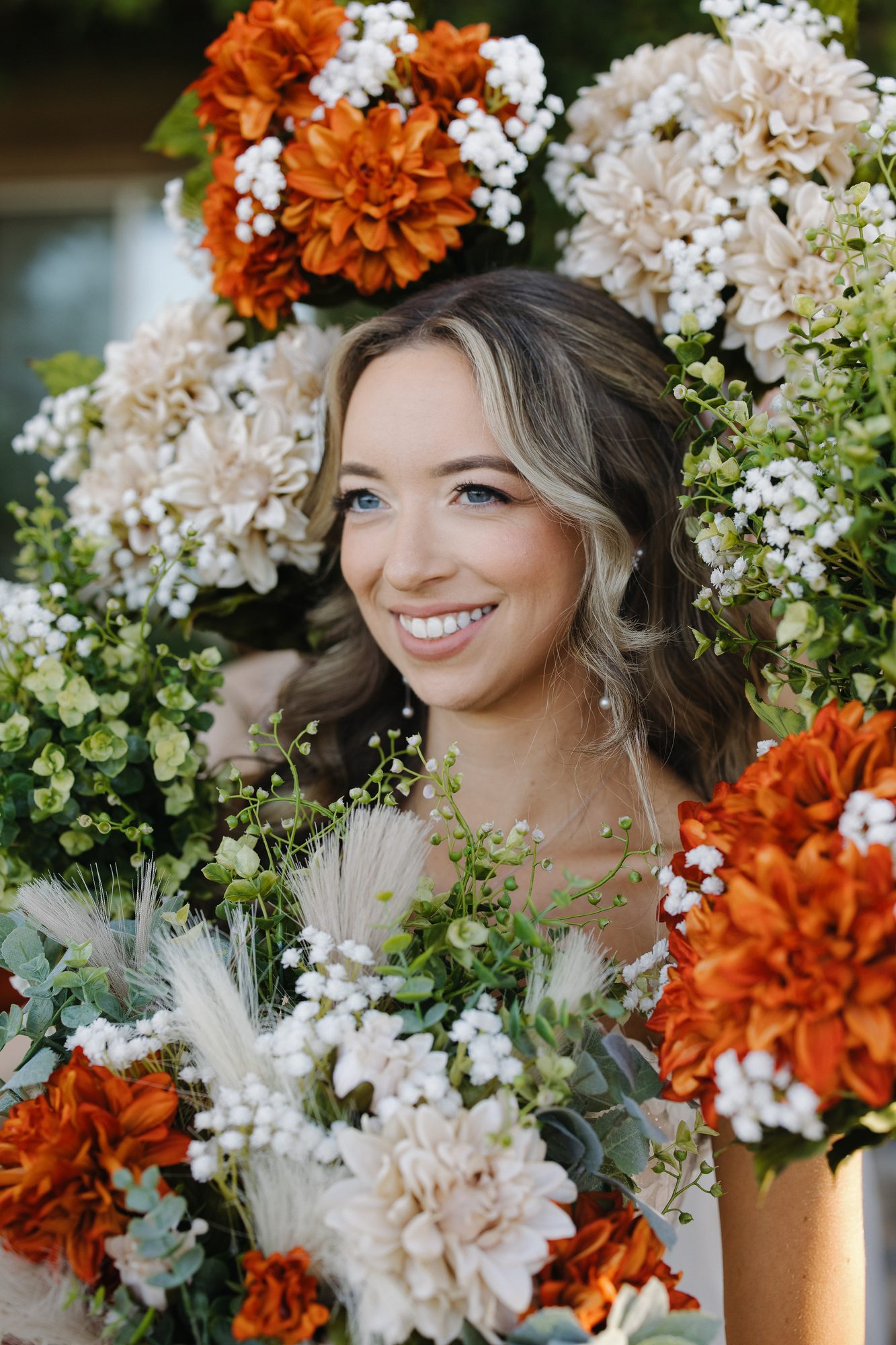 Smiling bride with soft waves surrounded by white and orange flowers on her wedding day.