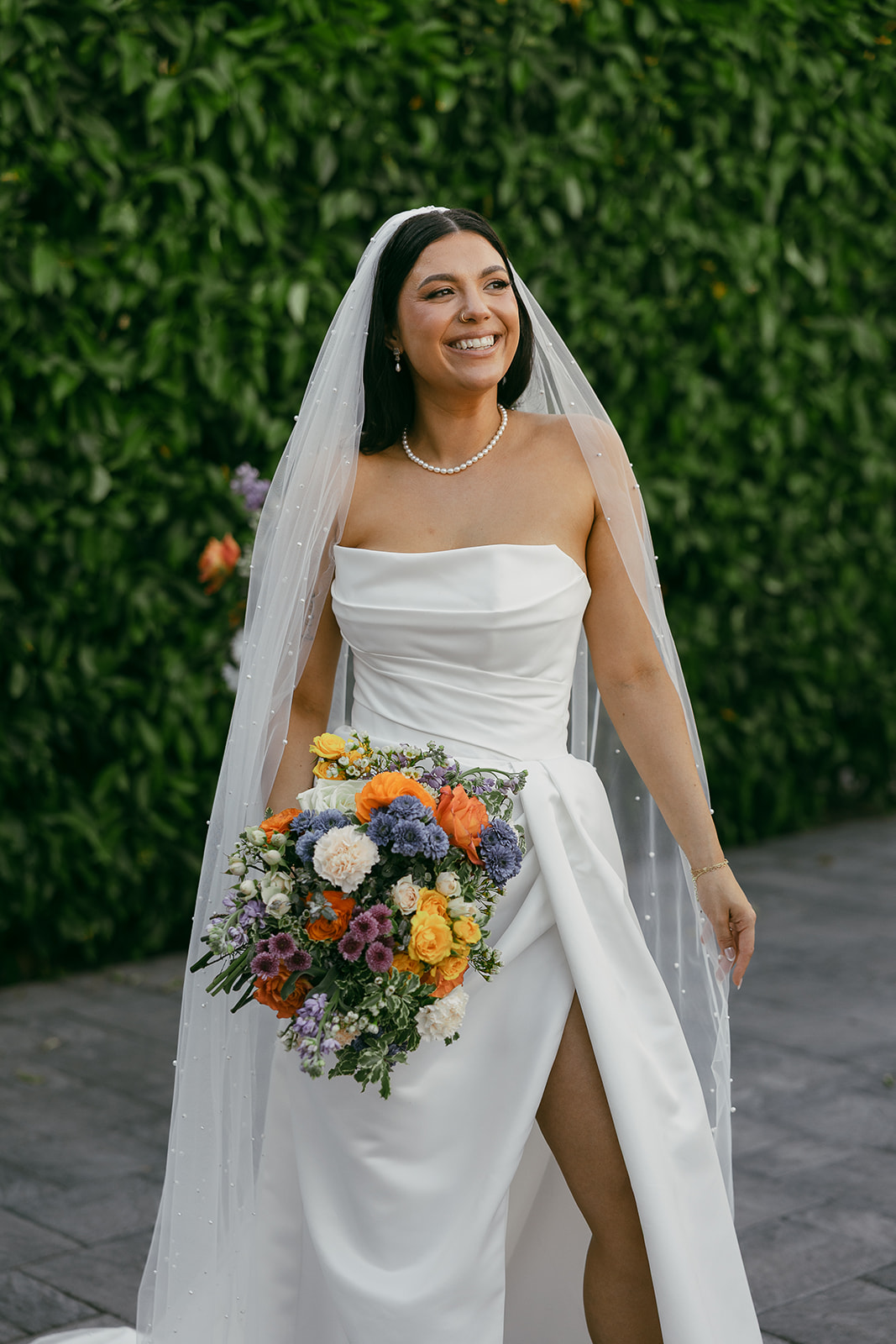 Smiling bride in a strapless gown and veil holding a colorful bouquet